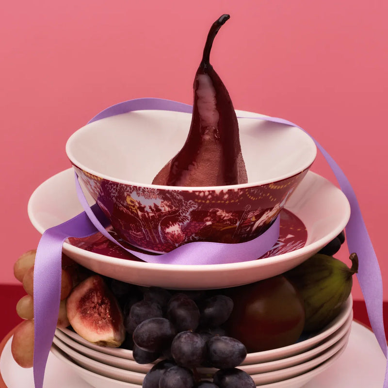 Stack of stacked bowls with a pear inside, surrounded by fruits on a pink background