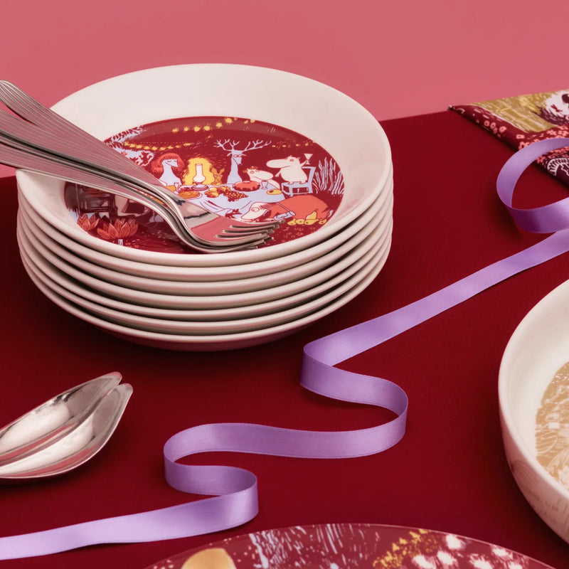 Stack of decorative plates with a red design on a red surface with a purple ribbon.