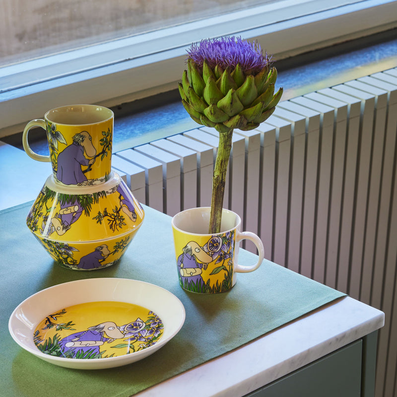 Yellow ceramic pitcher, mug, and plate with purple floral design on a green surface.
