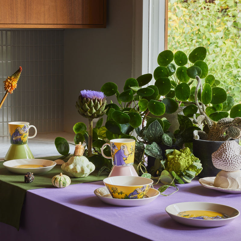 Decorative table setting with plants, colorful teacups, and a window in the background.