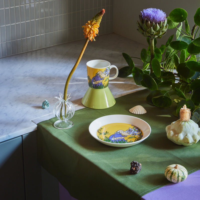 Decorative items including a mug, plate, and small plants on a green surface with a tiled wall background.