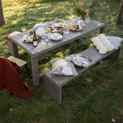 Outdoor setting with a table and bench in a grassy area, featuring food and drinks.