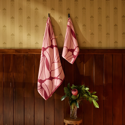 Two pink patterned towels hanging on a wooden wall with a vase of flowers below.