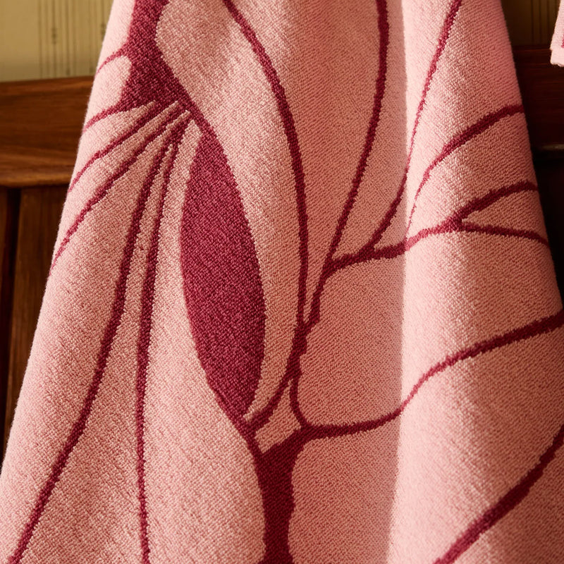Close-up of a pink fabric with leaf-like patterns on a wooden surface.