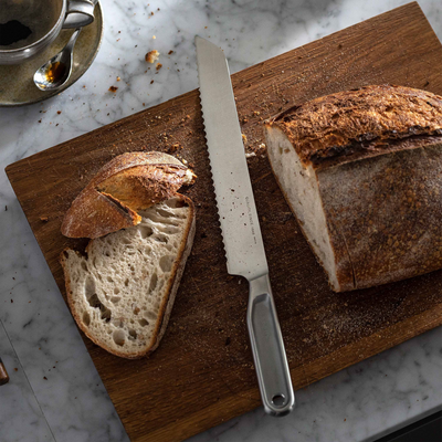 Loaf of bread with a slice cut, knife, and coffee on a wooden cutting board.