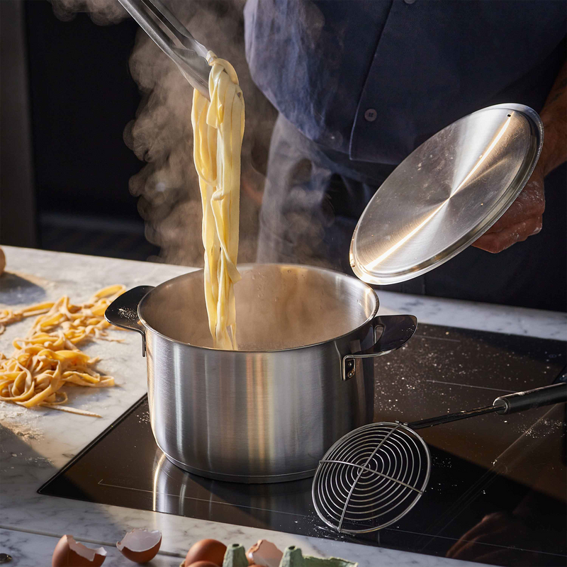 Cooking pasta being added to a pot on a stove with steam rising.