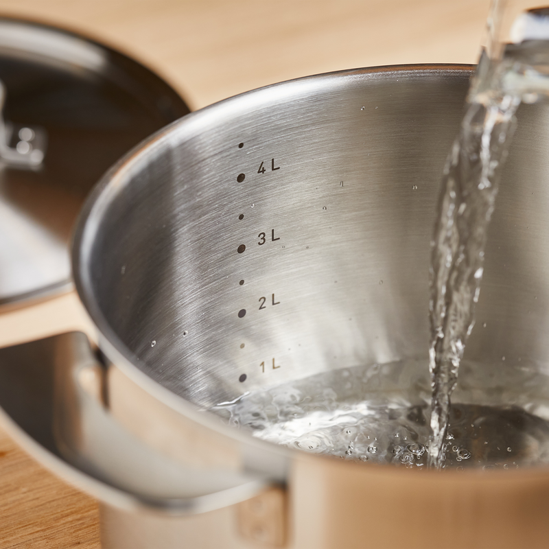 Metal measuring cup with water being poured into it, showing measurement markings.