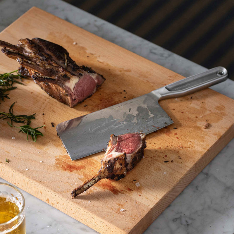 Sliced lamb on a wooden cutting board with a knife and a glass of beer.