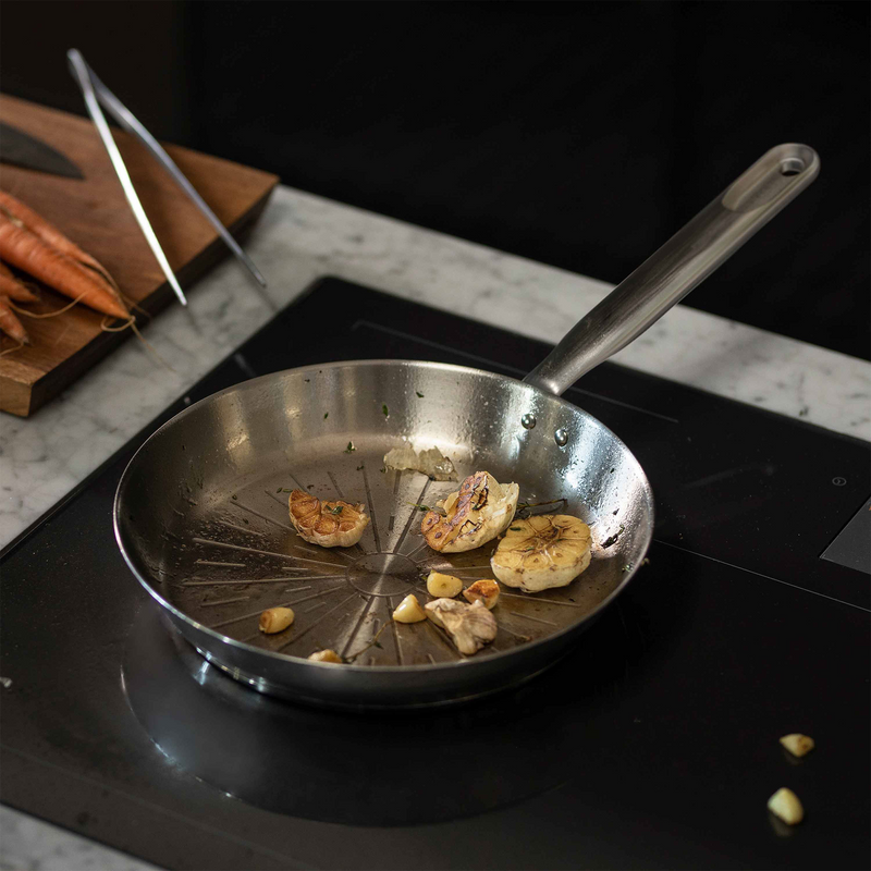 Stainless steel frying pan with garlic cloves on a stovetop