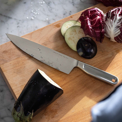 Knife on a wooden cutting board with vegetables on a marble surface