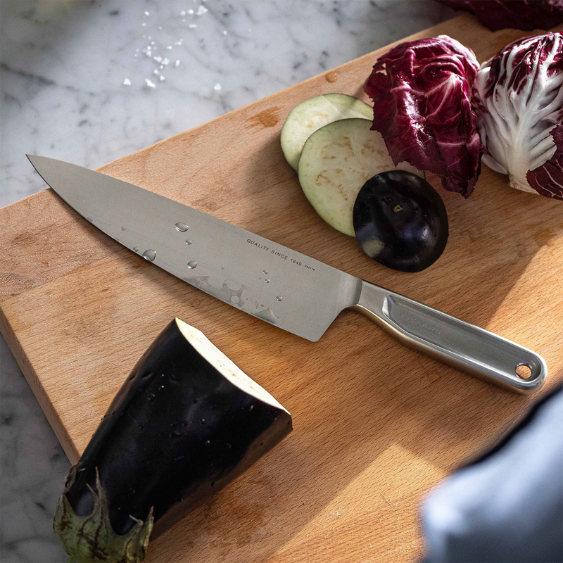Knife on a wooden cutting board with vegetables on a marble surface