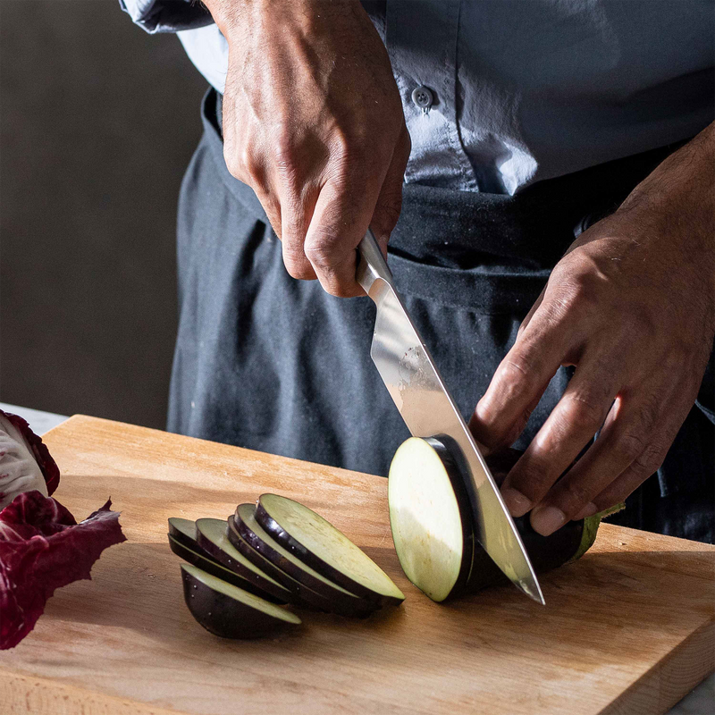 Person slicing an eggplant on a wooden cutting board with a knife.
