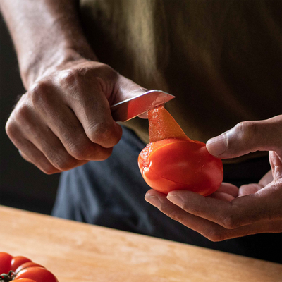 Person peeling a tomato with a knife on a wooden surface