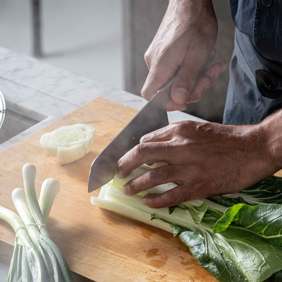 Person chopping vegetables on a wooden cutting board with a knife.