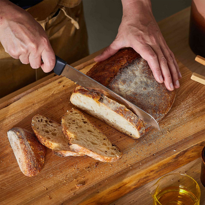 Person slicing a loaf of bread on a wooden cutting board with a knife.