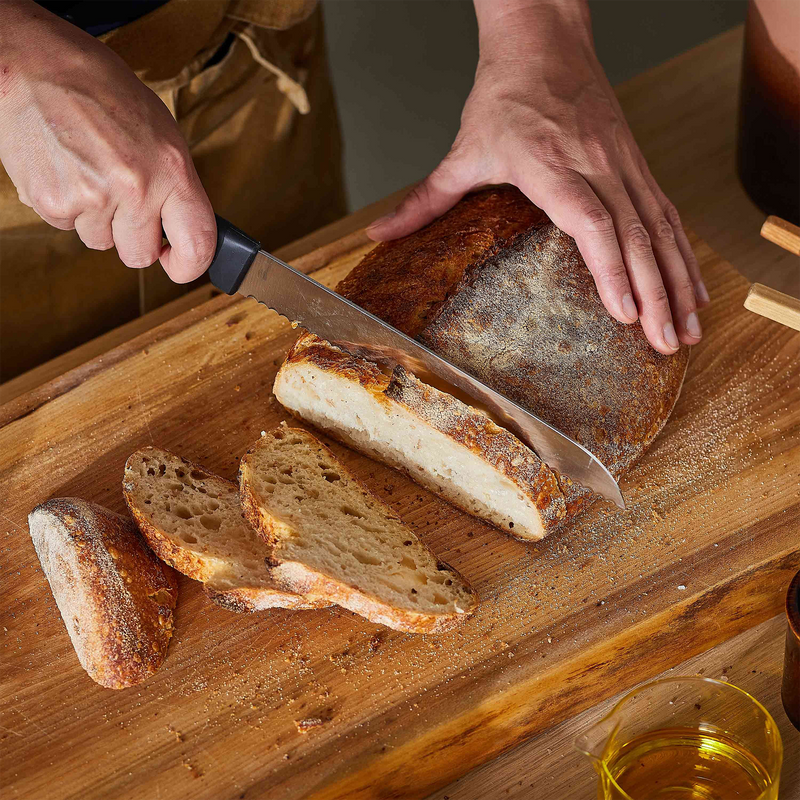Person slicing a loaf of bread on a wooden cutting board with a knife.