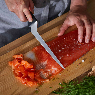 Person filleting a salmon on a wooden board with a knife.