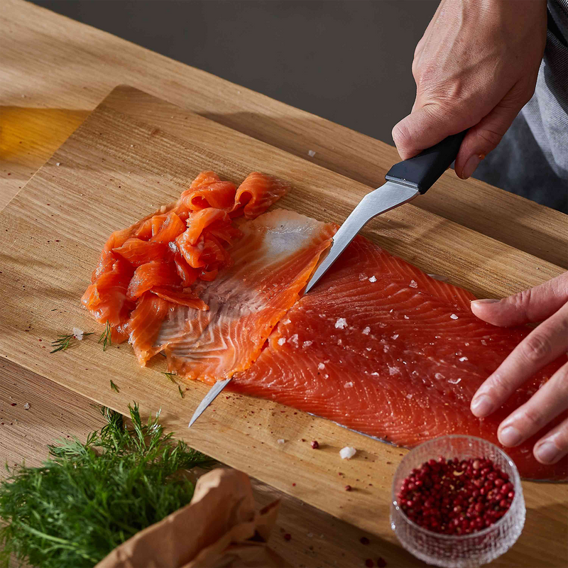 Person cutting a piece of salmon on a wooden cutting board with a knife.