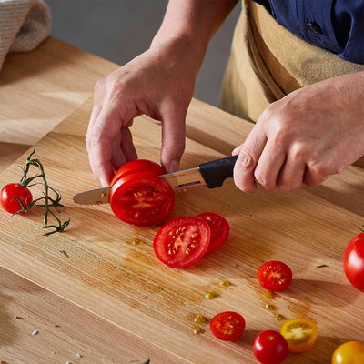 Person slicing tomatoes on a wooden cutting board with a knife.