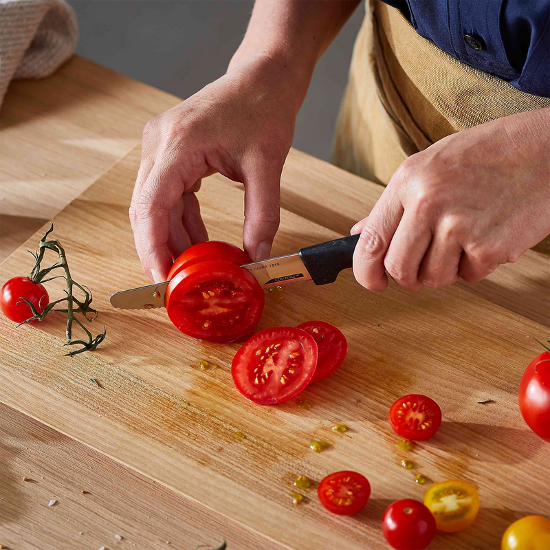 Person slicing tomatoes on a wooden cutting board with a knife.