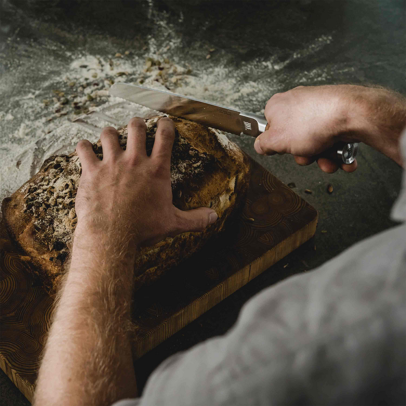 Person slicing bread on a wooden cutting board with a knife.