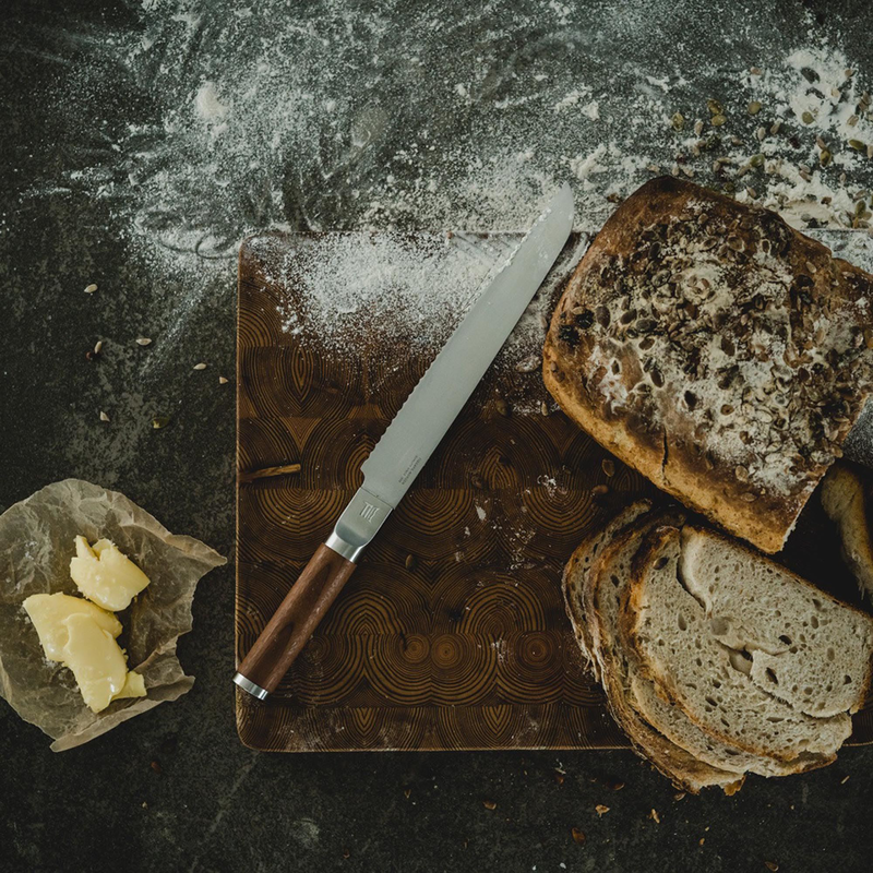 Sliced bread on a wooden cutting board with a knife and butter, on a dark surface.