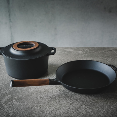Black pot and frying pan with wooden handles on a gray surface