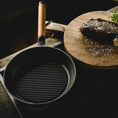 Black grill pan on a stovetop with a wooden cutting board in the background