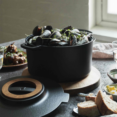 Black pot with greens on a table with bread and other dishes