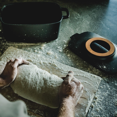 Person kneading dough on a floured surface with a black pot and electric stove in the background.
