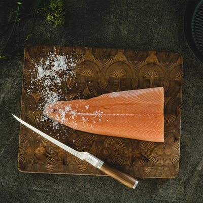 Raw salmon fillet on a wooden cutting board with salt and a knife.