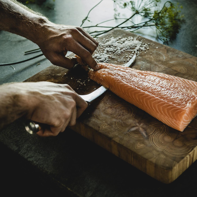 Person preparing salmon on a wooden cutting board with a blurred background