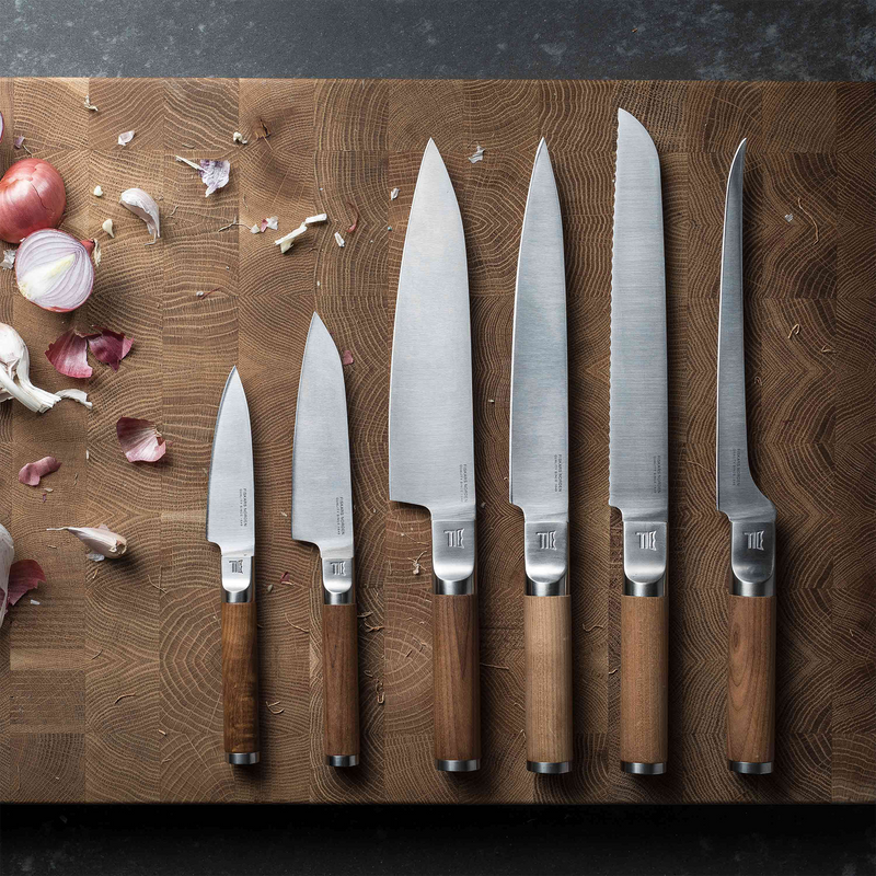 Set of knives with wooden handles on a wooden cutting board with vegetables.