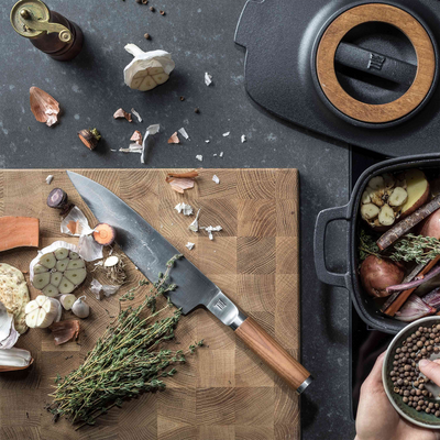 Butcher knife on a wooden cutting board with cooking ingredients and utensils.