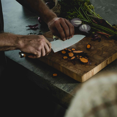 Person cutting vegetables on a wooden cutting board with a knife.