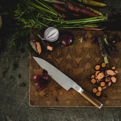 Chef's knife on a wooden cutting board with vegetables around