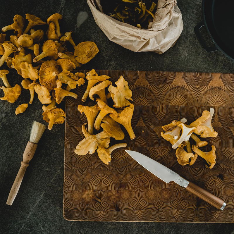 Chanterelle mushrooms on a wooden cutting board with a knife and a basket in the background.