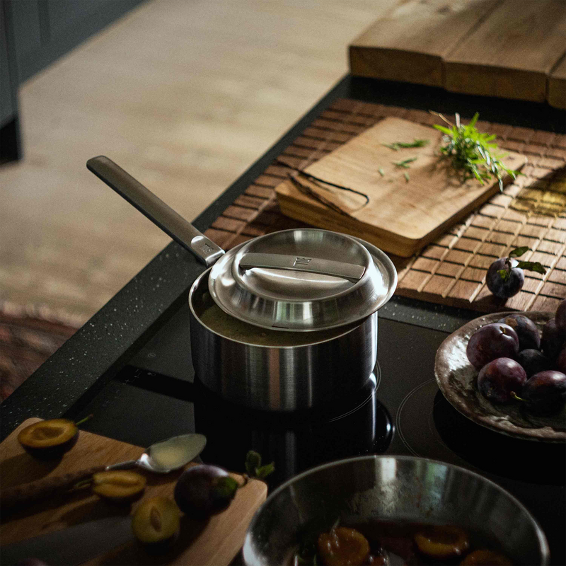 Stainless steel pots on a kitchen stove with wooden cutting boards and plums in the background