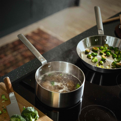 Two pots on a stovetop with vegetables being cooked, one pot contains boiling water and the other has sautéed brussels sprouts.