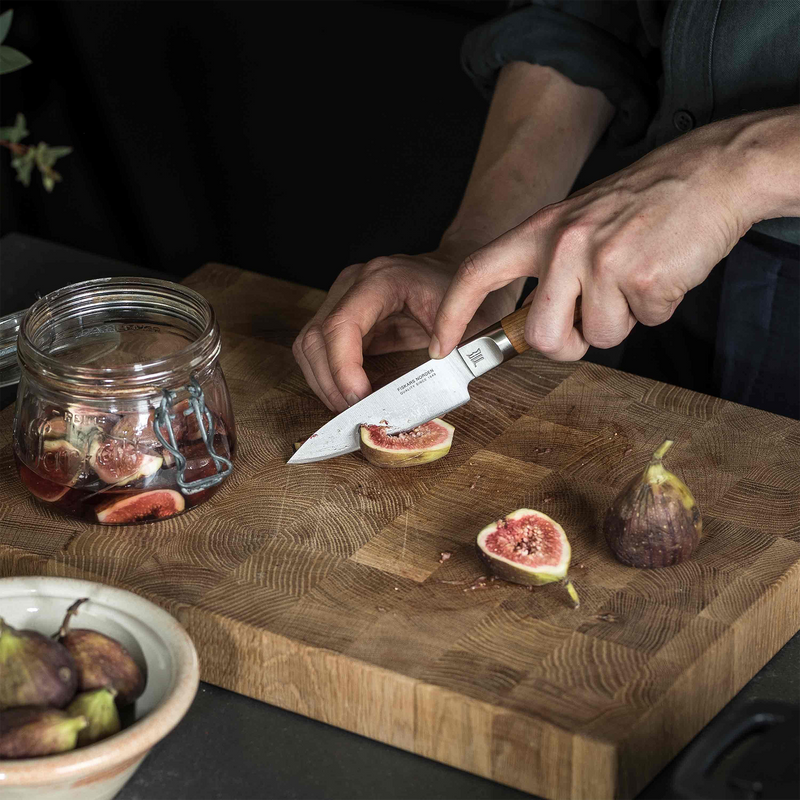 Person cutting figs on a wooden cutting board with a knife.