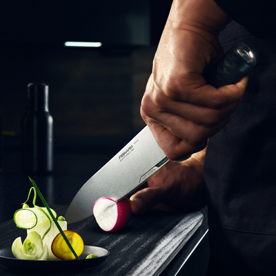 Person holding a chef's knife over a cutting board with vegetables, in a kitchen setting.