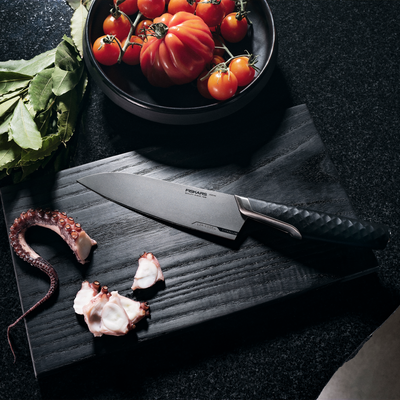 Forked knife on a dark surface with tomatoes and octopus pieces
