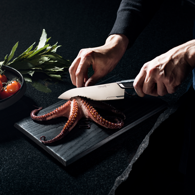 Person cutting an octopus on a dark surface with a knife
