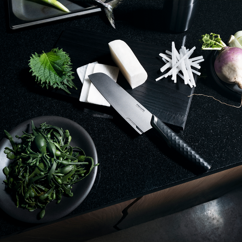 Knife on a black surface with sliced white radish and green leaves.