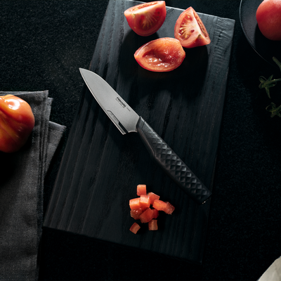 Knife on a dark surface with chopped tomatoes and whole tomatoes.