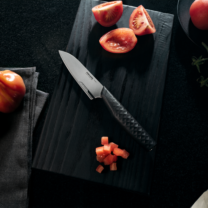 Knife on a dark surface with chopped tomatoes and whole tomatoes.