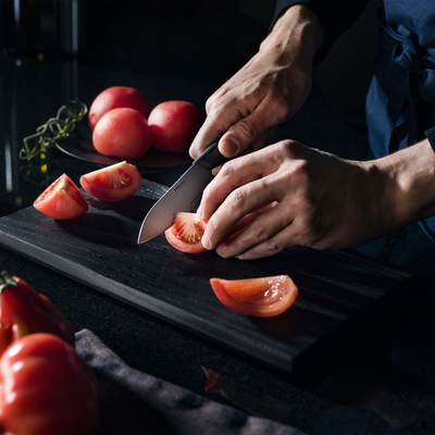 Person cutting tomatoes on a dark surface with a knife