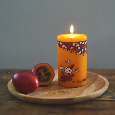 Orange candle with a design on a wooden plate with two plums against a gray background