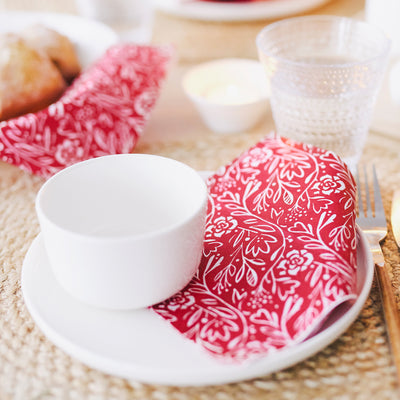 White cup and saucer on a red floral cloth with a fork on a wooden table.