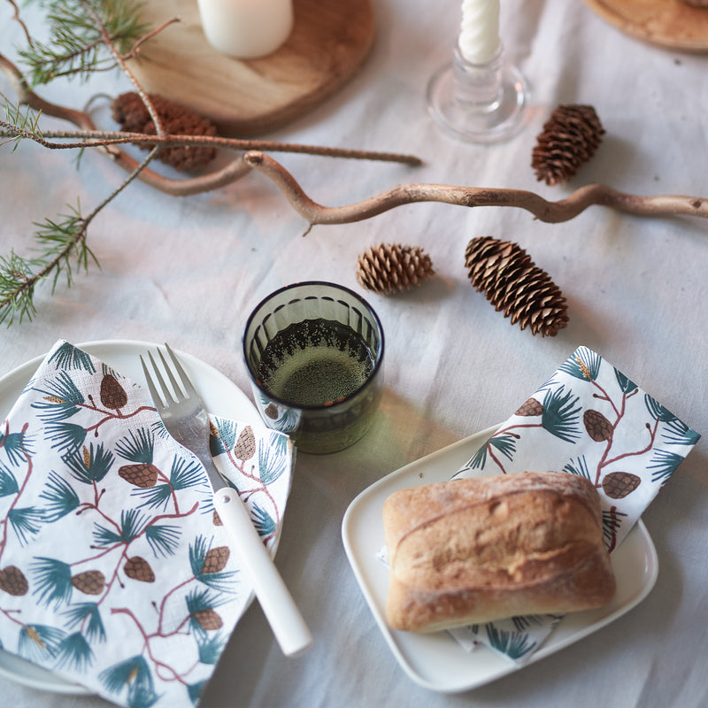 Table setting with bread, glass of juice, and decorative napkins on a white tablecloth.